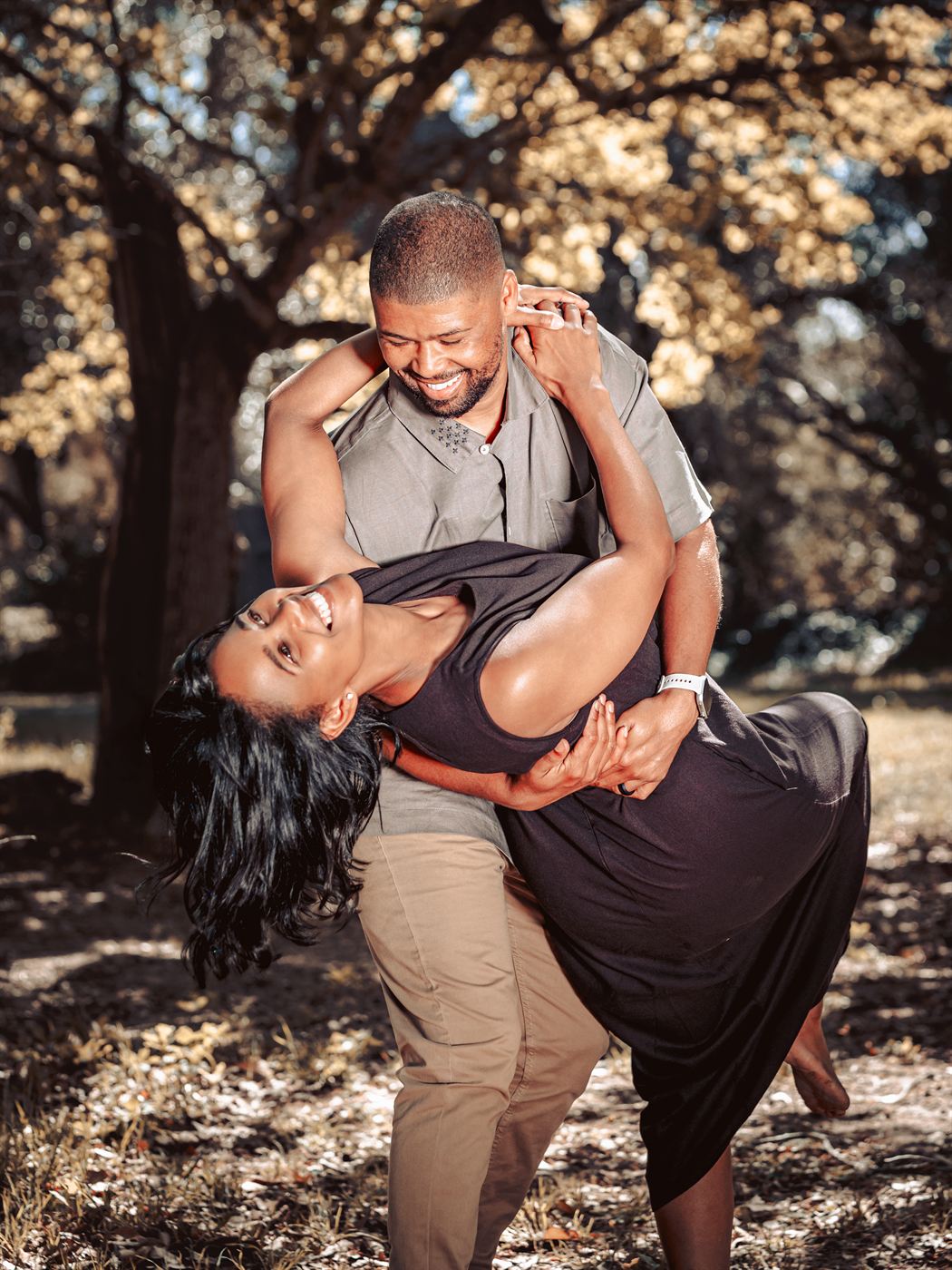 Couple caught mid-dance dip beneath dappled trees, both laughing