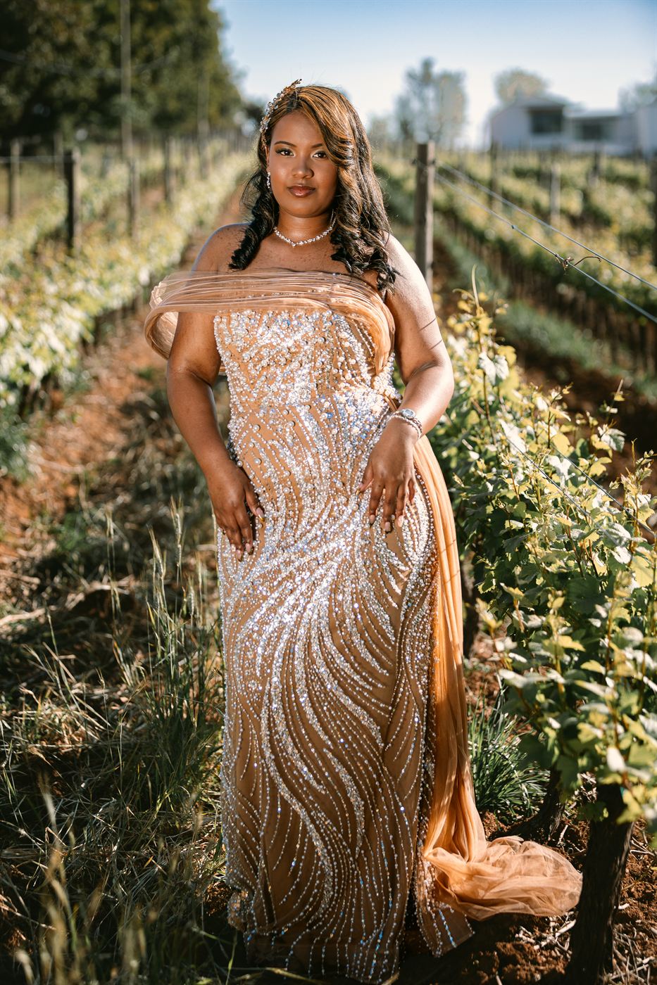 Young woman in a beaded gown standing between rows of vines